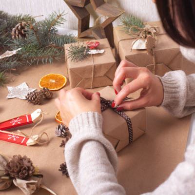 Woman wraps a Christmas present using brown craft paper with a fabric ribbon.