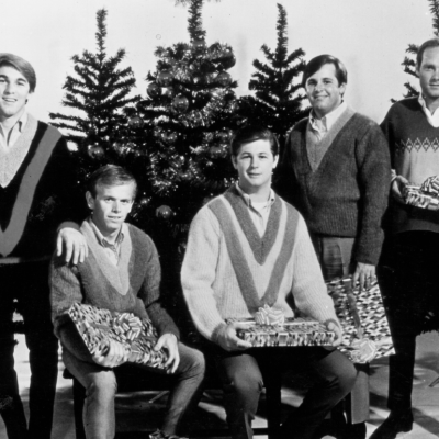 Rock and roll band "The Beach Boys" pose for a portrait in front of some Christmas trees holding presents in circa 1964.