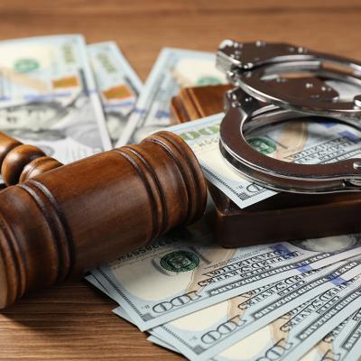 A closeup on a judge's gavel, money and handcuffs on a wooden table.