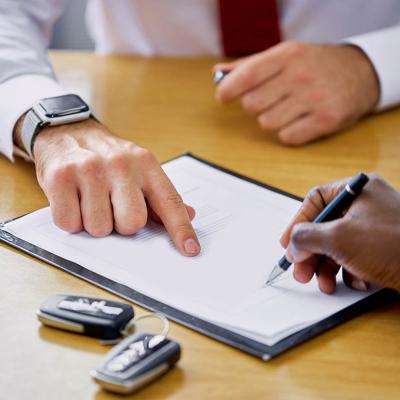 Close-up photo of hands and paperwork for financing a car with car keys visible.