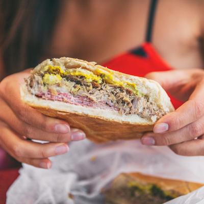 Closeup of a woman holding a Cuban sandwich at a typical local cafe outdoors. 