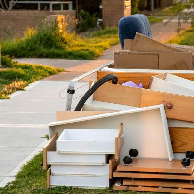 Discarded drawers, plywood furniture next to the sidewalk in morning light.