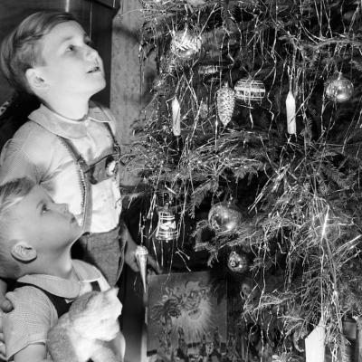 Kids look at a Christmas tree in their living room with candles on it in 1949.