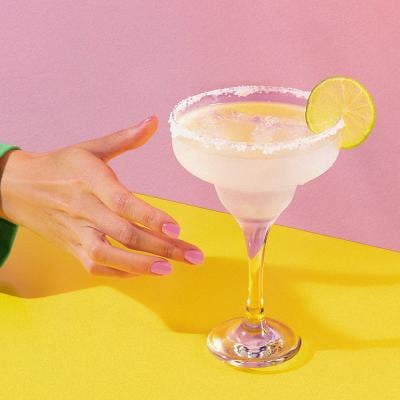 Hand reaching for lemon-garnished drink on a pink and yellow background. 