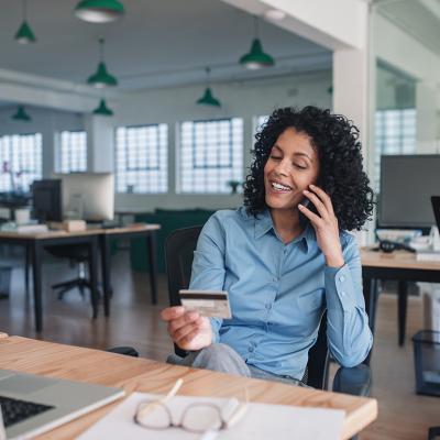 A young businesswoman smiling while on the phone and looking at her credit card.