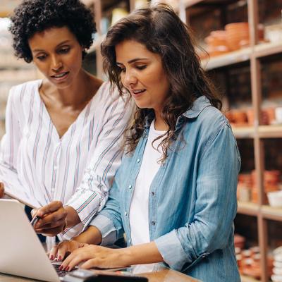 Two small business owners going through expenses, ceramics and products visible on shelves behind them.