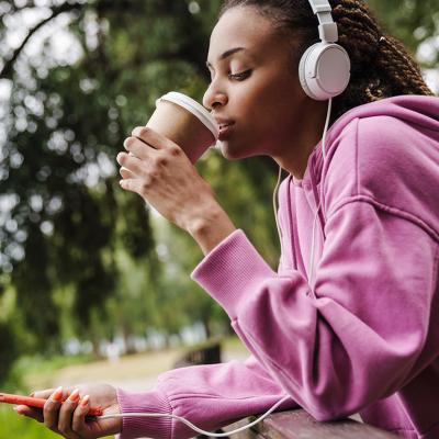 A woman taking a break from working out by drinking coffee while listening to music in the park.