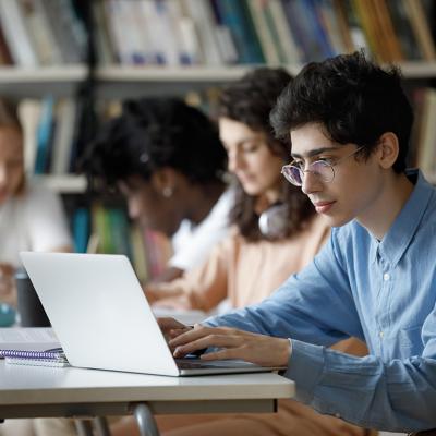 A row of students sitting at table in the library working on laptops.