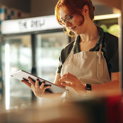 A small grocery owner using a digital tablet in her store.