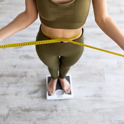 A woman on checking body measurements with a tape and checking weight on a scale.