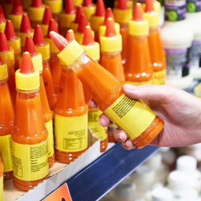 A customer choosing a bottle of hot sauce from its supermarket aisle.