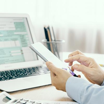 Businessman looking through phone and with a laptop is filling out a tax return form.
