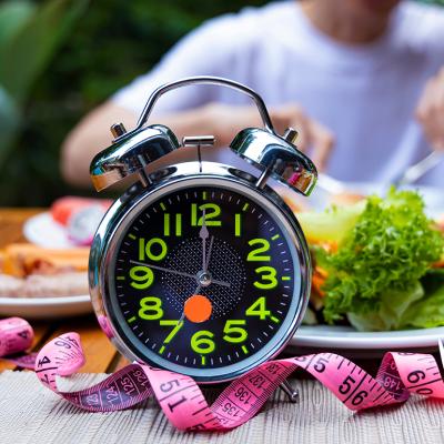 A clock stands in front of a man eating meals, practicing intermittent fasting.