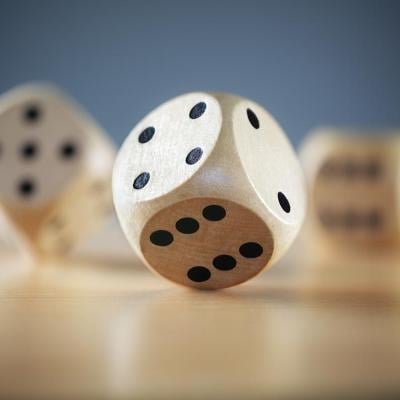 Close up of three wooden dice on a desktop, one in sharp focus, with a gray background.