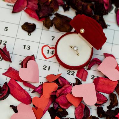 An engagement ring surrounded with rose petals on top of a calendar with February 14th circled.