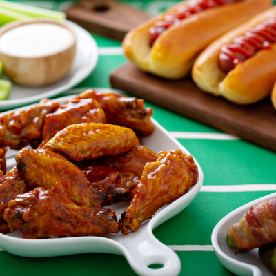 A table with glazed chicken wings, hot dogs, celery sticks and dip