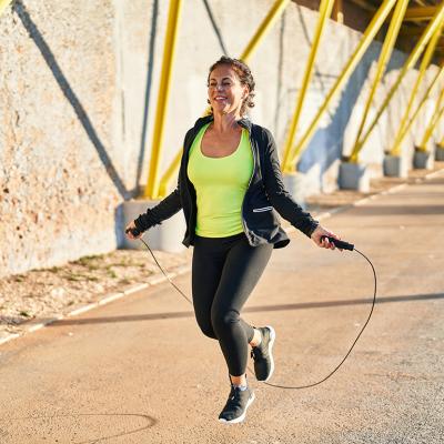 Middle-aged hispanic woman working out outdoors using a jumping rope.