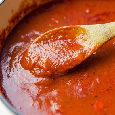 A thick, rich and slow-cooked marinara sauce being stirred in a Dutch oven.