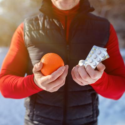 Cropped view of a sportsman holding an orange and pills outside during winter season.