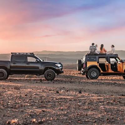 An AWD and a 4WD vehicle on a wide park lot with its passengers watching sunset.