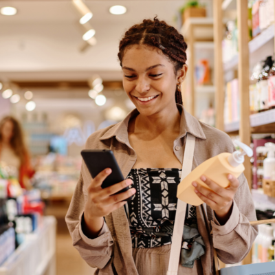 A smiling woman in a store, holding a bottle with a pump and looking at her phone. 