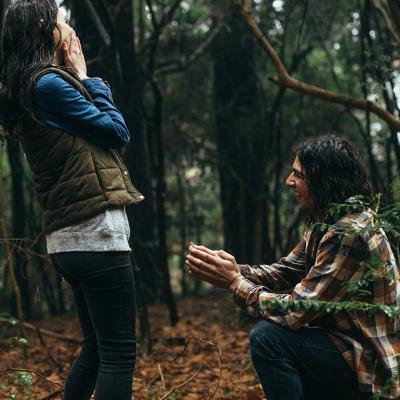 A man proposes to his partner during a rain in a natural location.