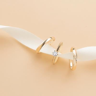 A white ribbon holds three types of different wedding rings.