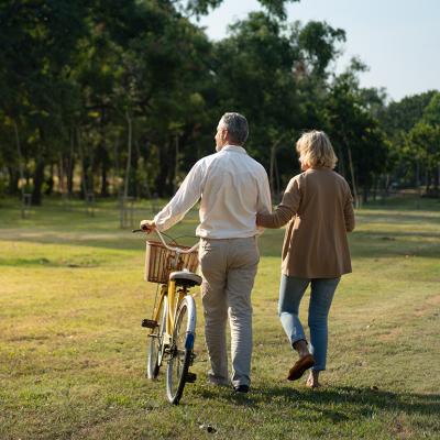 A middle-aged couple taking a stroll in a wide park with a bike.