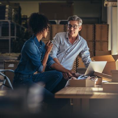 Two business partners having a discussion and using a laptop to check information.