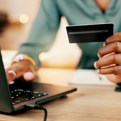 A female employee holding a company card for a transaction using a laptop.