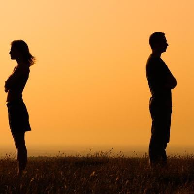 Concept of relationship difficulties shown through silhouettes of two people facing away from each other with orange sunset-colored background.