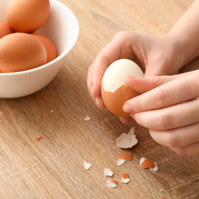 A person's hands peeling boiled eggs over a wooden countertop