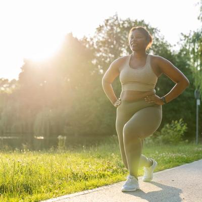 Woman doing a lunge in a park, backlit by sun with grass in the background.