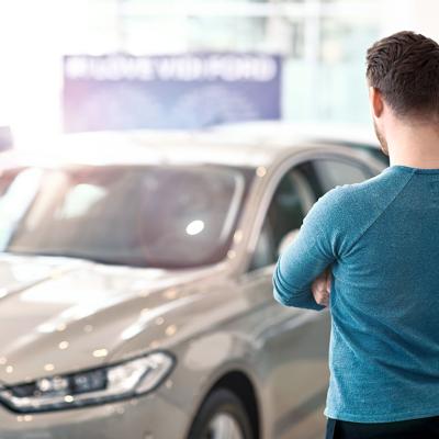 A pensive man looking at a car in a dealership.