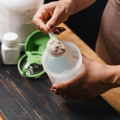 A spoonful of creatine powder being put into a shaker.