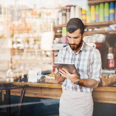 A coffee shop owner using his tablet by the counter.