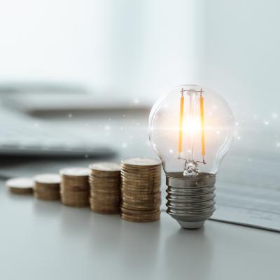 A light bulb and rows of coins decreasing against the background of financial reports as a concept of reducing tax costs.