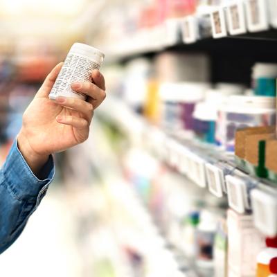 A customer carefully reviewing bottle of medicine from an aisle during a purchase.