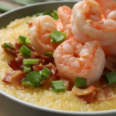 A bowl of freshly made grits topped with shrimp, bacon bits and sliced scallions