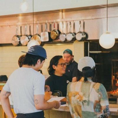 Customers and staff of an open-kitchen restaurant mingle.