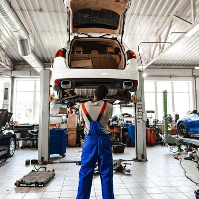 A pensive mechanic in a car service looking up a lifted car for repair.