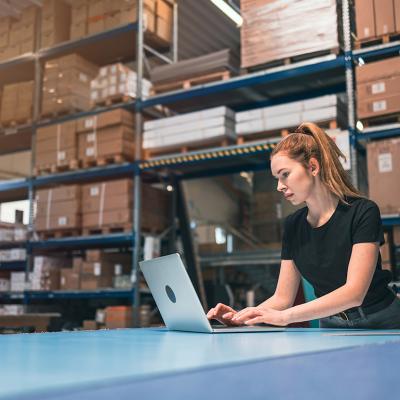 A woman managing logistics and using a laptop in a warehouse.