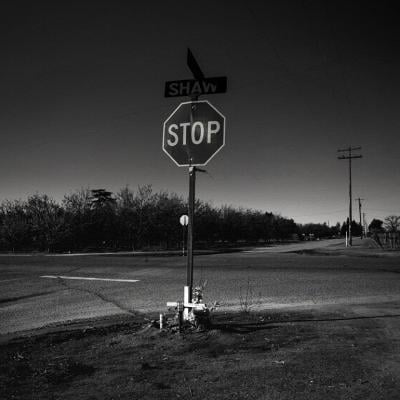 A black and white photo of a stop sign in the middle of an empty intersection.