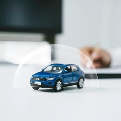 Miniature figure of a blue car with a shield illustration for insurance.