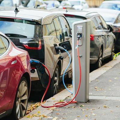 A lane of electric cars being charged on the side of a street.