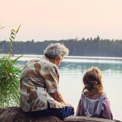 Grandparent sits with grandchild, overlooking the river on a warm day.