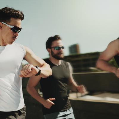 Three men on a fitness run and one of them is looking at his smartwatch for tracking.