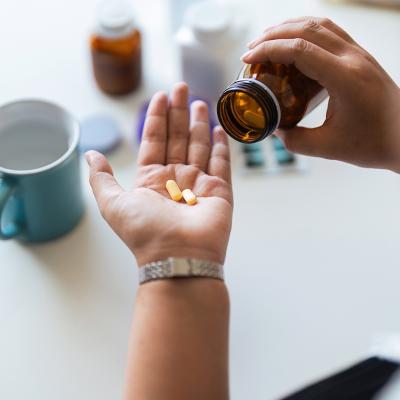A woman's hand catching vitamin tablets from its bottle for daily intake.