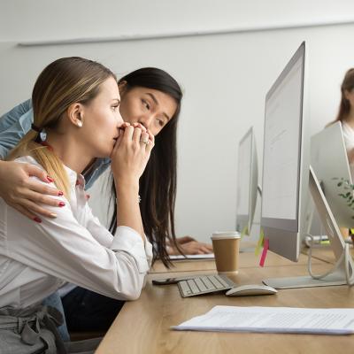 A woman at work reading bad news from email and her colleague is holding her for support.