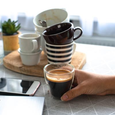 Person holding a full glass of coffee on a background of multiple empty finished cups.
